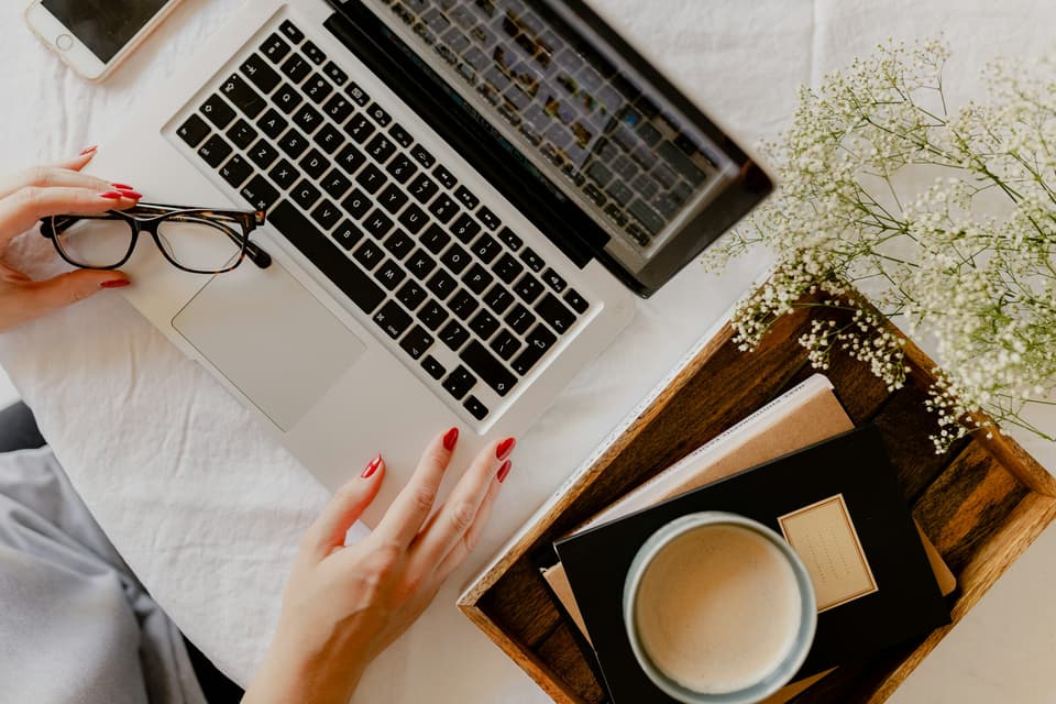 Hands at a laptop, with a coffee and a notebook alongside