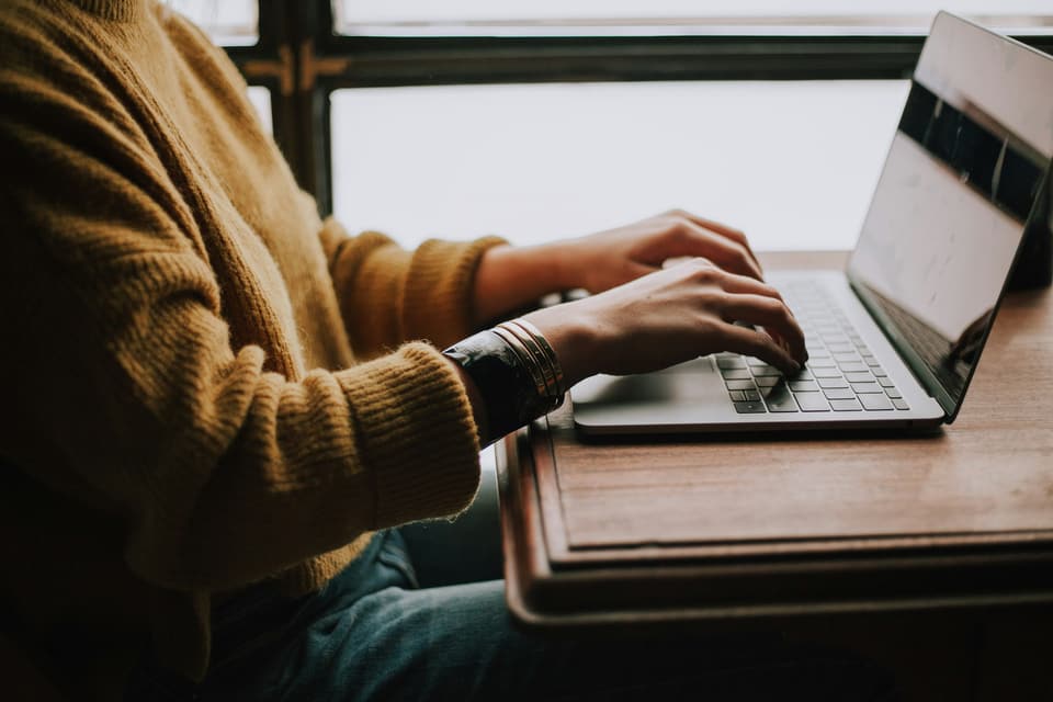 A person typing on a laptop by a window